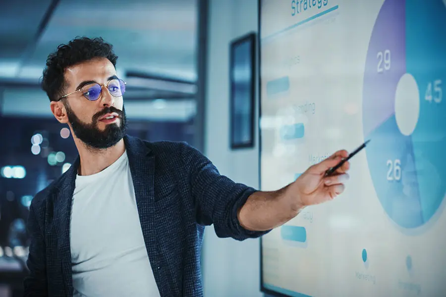 A professional is shown in front of a presentation screen sharing business analytics data, demonstrating the skills acquired from an online master's in business analytics. 